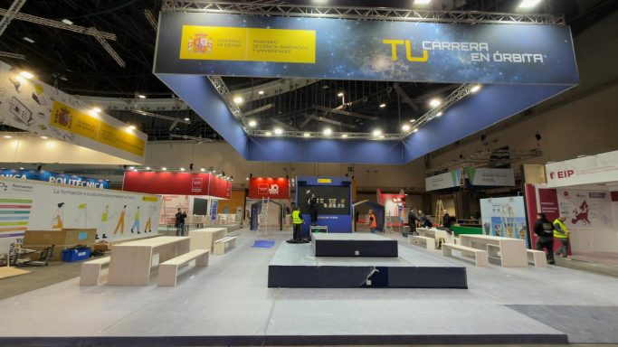 AULA IFEMA 2026 Stand de exhibición en construcción con trabajadores y áreas delimitadas.